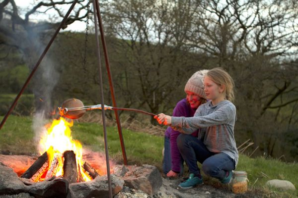 A photo of a mother and daughter cooking popcorn over a campfire in the glamping field