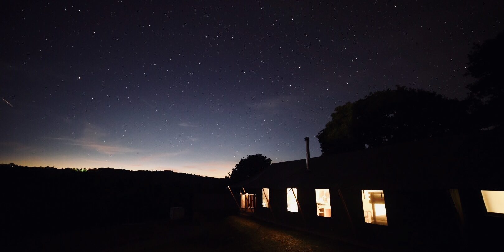 A night time image of the valley, a tent to the right and a shooting star to the left of the picture