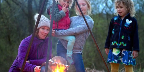 A photo of a mother and children cooking around the campfire in the glamping field